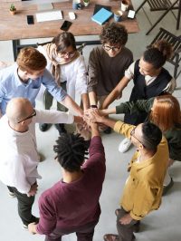 A diverse group of professionals joins hands in a team-building exercise indoors.